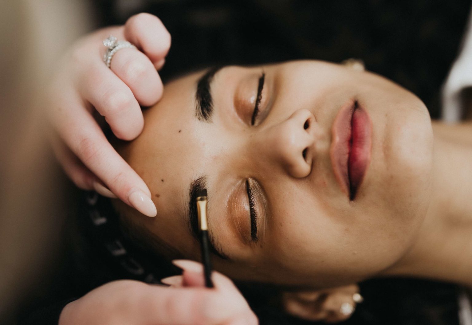 a woman lying down eyes closed receiving a brow tint
