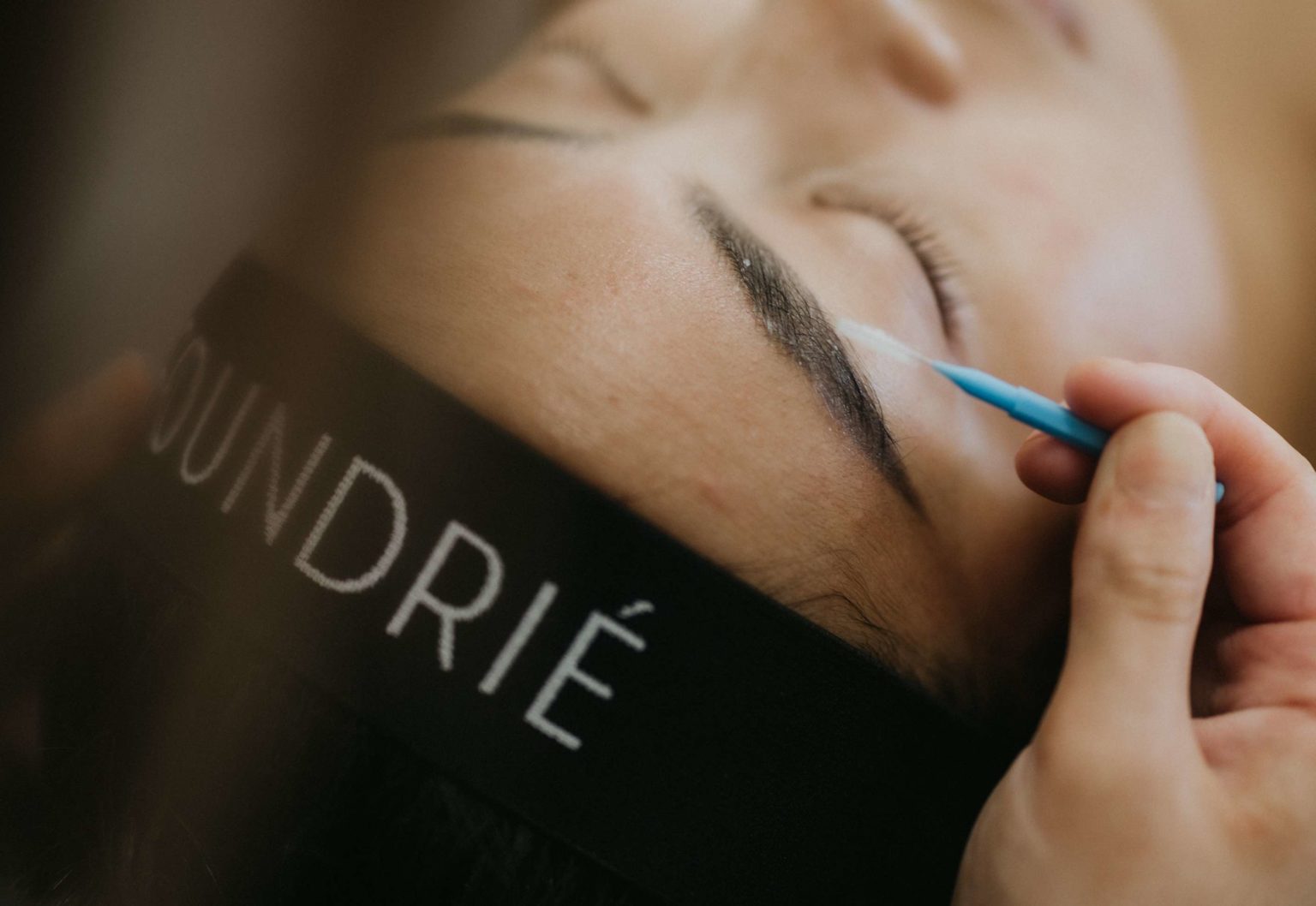 a woman lying down eyes closed receiving a brow tint