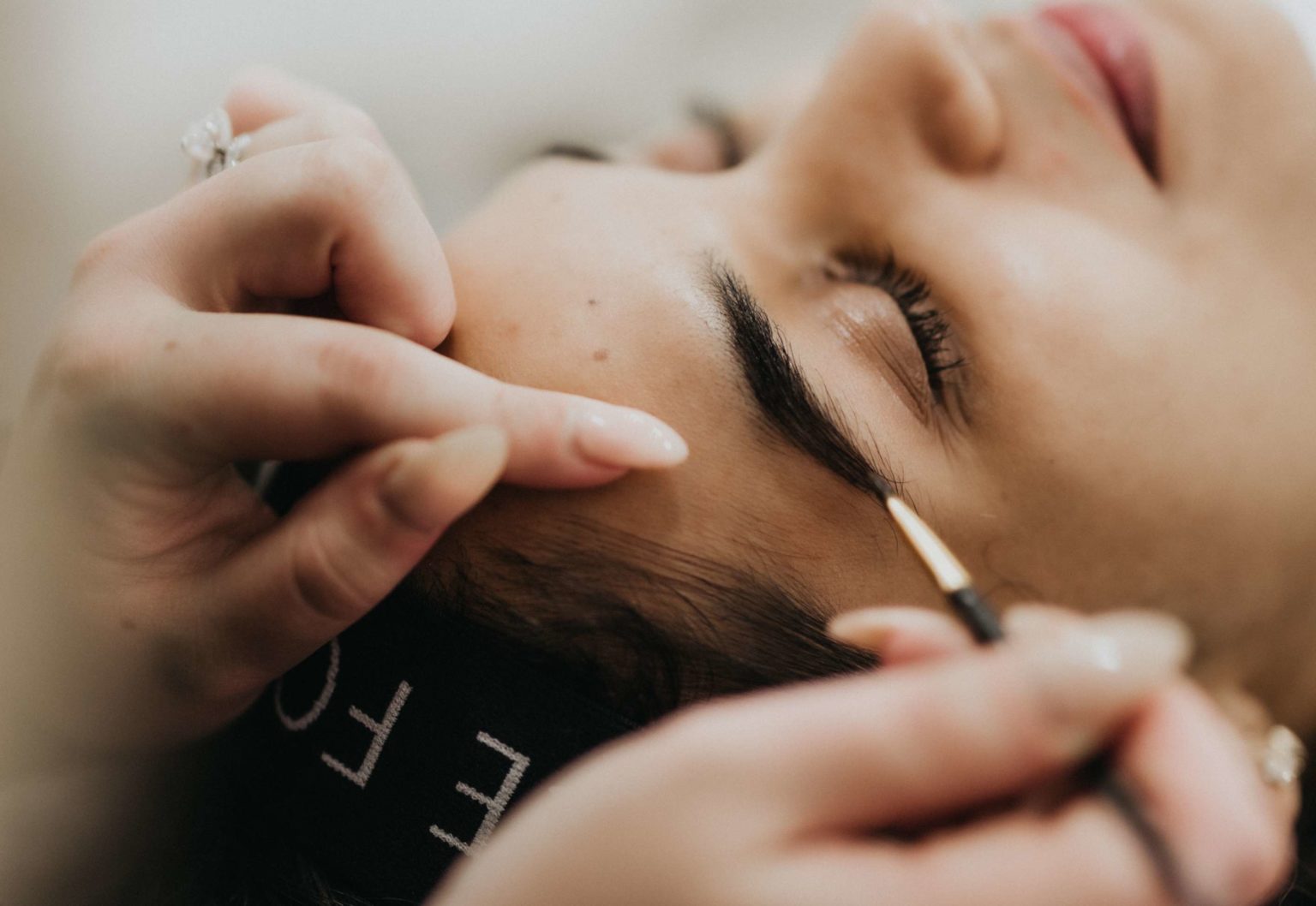 a woman lying down eyes closed receiving a brow tint