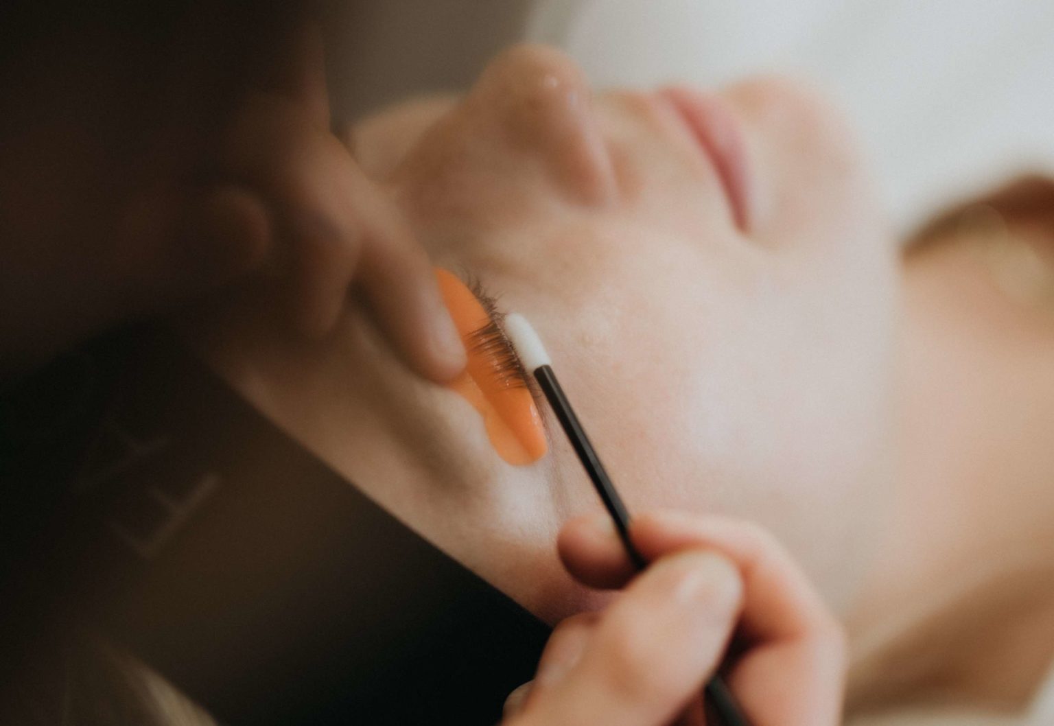 a woman lying down eyes closed receiving a brow tint